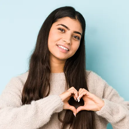 Teenager with dark brown hair and eyes making a heart symbol with her hands